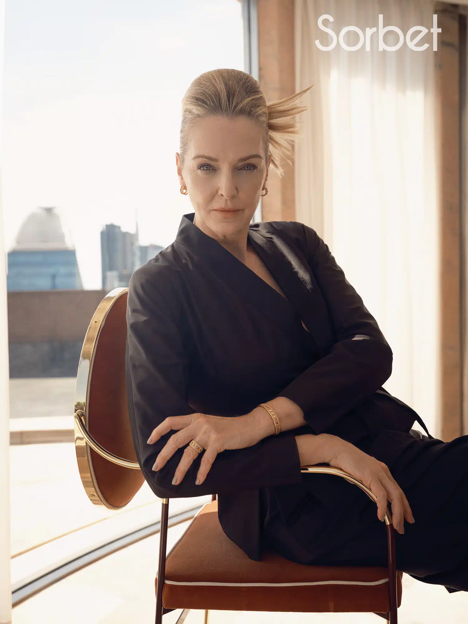 woman sitting on a brown leather chair with the backdrop of Milan's skyline is in the background wearing Dior jewelry and Dior clothes