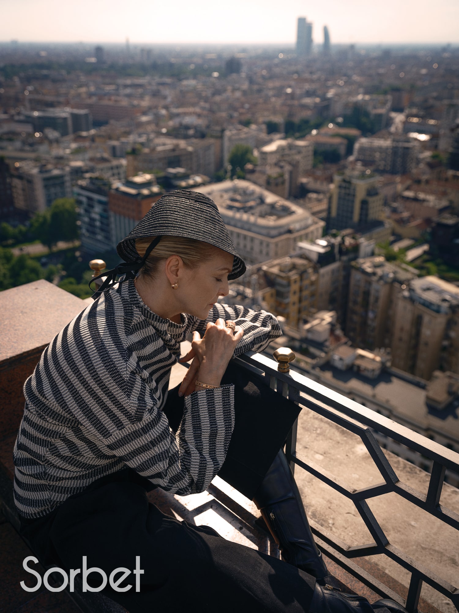 woman laying over a balcony with the Milanese skyline is a backdrop wearing Dior jewelry and Dior fashion