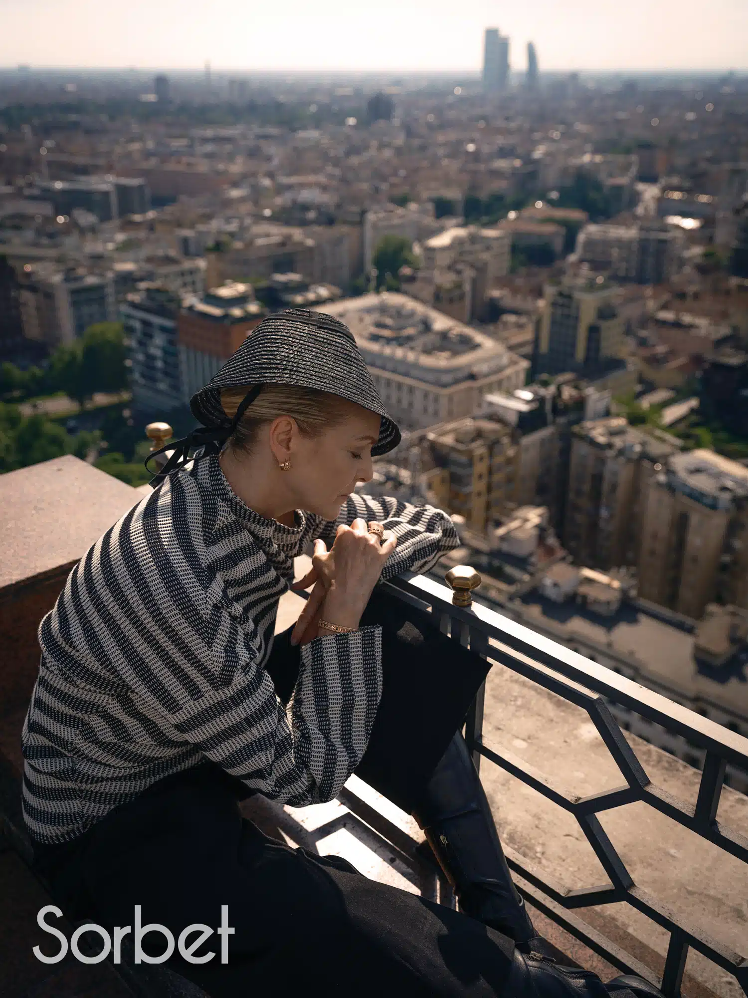 woman laying over a balcony with the Milanese skyline is a backdrop wearing Dior jewelry and Dior fashion