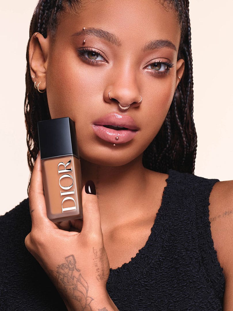 Willow Smith featured on the campaign for Dior Beauty holding a bottle of Dior Forever Foundation against her face, showcasing a radiant complexion and facial piercings.