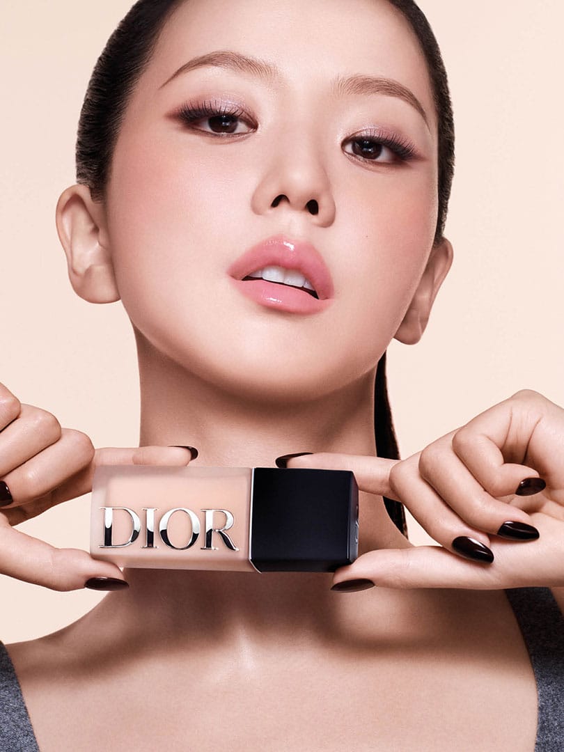 Jisoo holding a bottle of Dior Forever foundation with both hands, showcasing a radiant makeup look