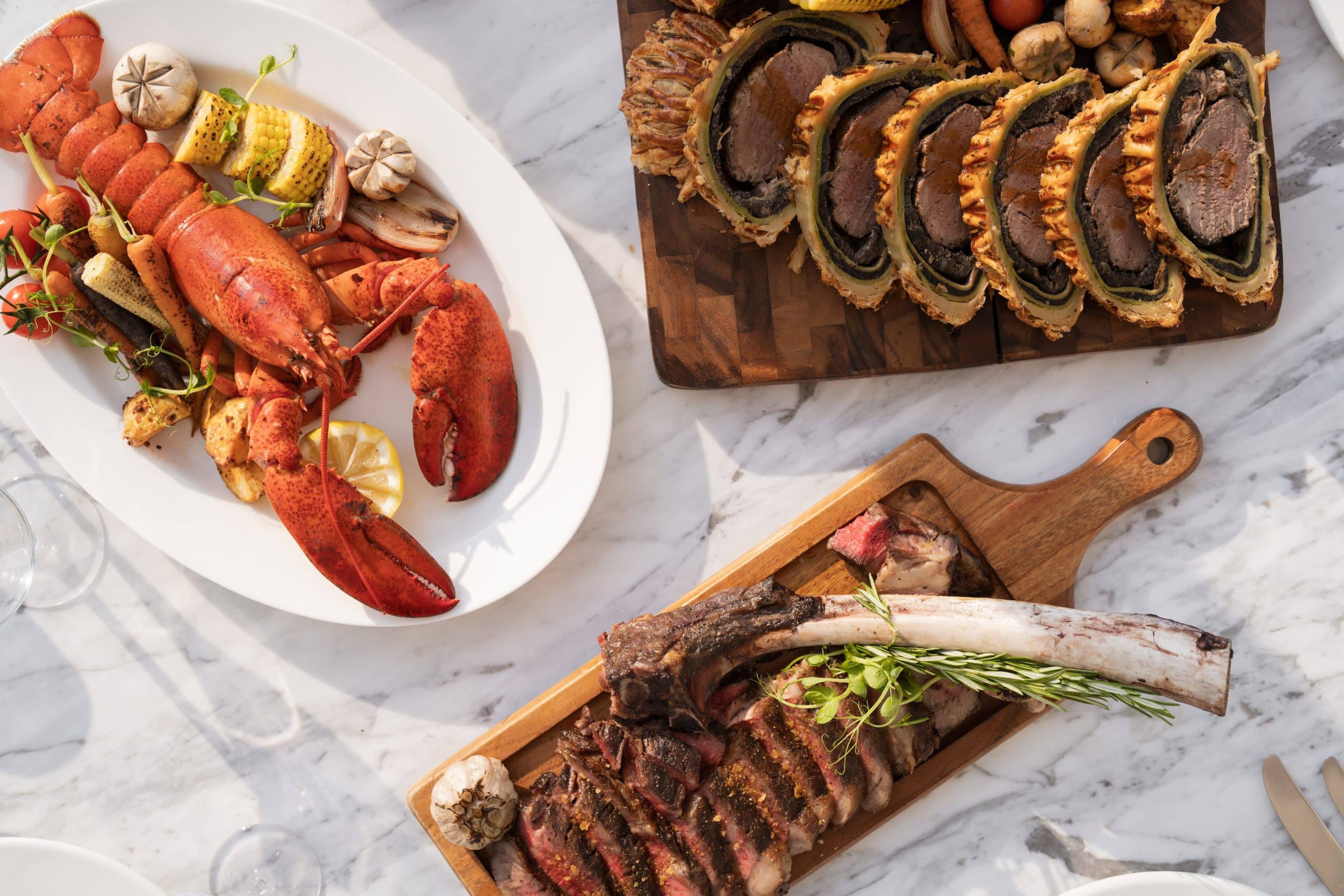 Luxury Easter Brunch at Traiteur Brunch Dubai Creek Resort featuring whole grilled lobster, Beef Wellington, and a Tomahawk steak on a marble table for the Sorbet Easter Guide 2026.