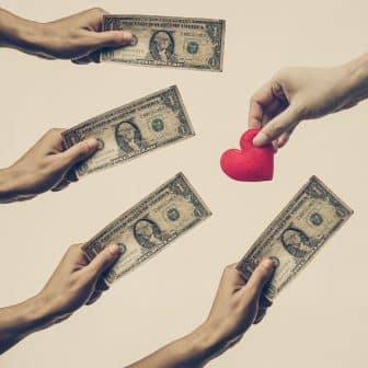 Male hand holding a dollar banknote trying to buy a red hearts from female hand - Buying love concept