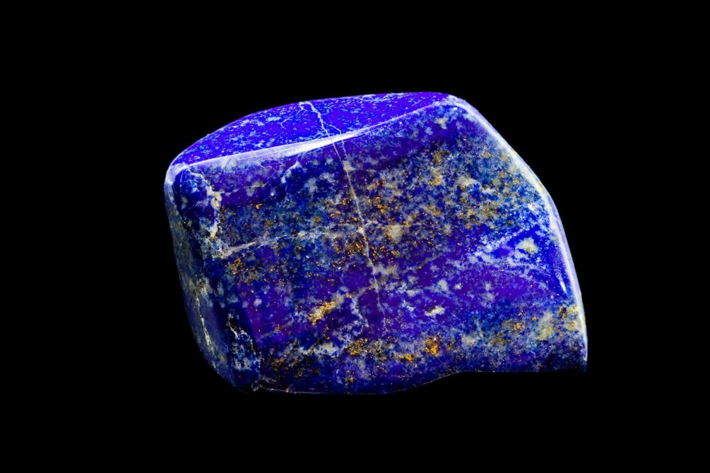 Blue shiny polished lapis lazuli stone specimen with golden inclusions, against black limbo background